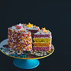 a cake sliced with 4 layers pink, orange, yellow and purple decorated with sprinkles and edible stars in the same colours by Karlik Pastry