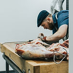 A butcher preparing meat on a butcherblock counter by Rolling Acres Fine Meats