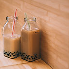 2 glass bottles filled with black milk tea with tapioca pearls in front of a wood backdrop from Bubbly T