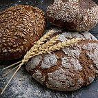 Several Sourdough loaves on a flour dusted board with sprigs of whole grain by Artisan Bread
