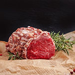 An uncooked roast of beef covered in bacon garnished with fresh rosemary from Halenda's Meats