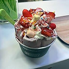A cup of rolled ice cream topped with fresh strawberries sprinkles and marshmellows