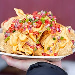 a plate of delicious nachos topped with cheese sauce, jalapeno pepper, tomatoes, and onion by Ray Woodley’s Craft Chippery